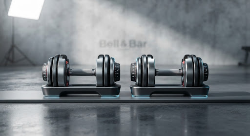 Two professional adjustable dumbbells on a polished dark floor with crisp editorial lighting.